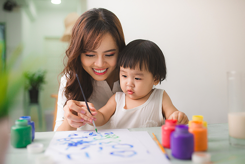 Happy family mother and daughter together paint. Asian woman helps her child girl.