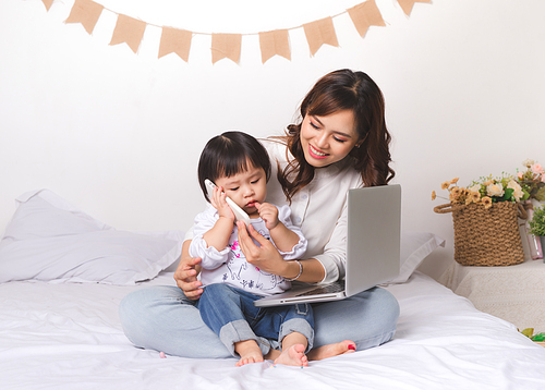 Asian lady in classic suitvworking on laptop at home with her baby girl chatting with father.
