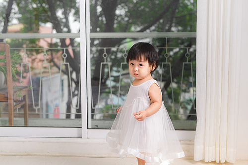 Little cute asian baby girl playing near the window at home