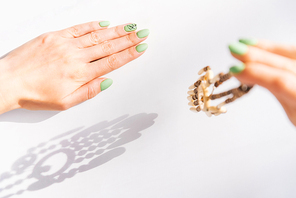 Woman’s hands with art leaf nails design and green manicure holding wooden handmade necklace.