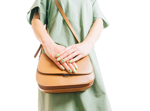 Unrecognizable young woman with summer style manicure in green dress standing with brown handbag. Female beauty and fashion.