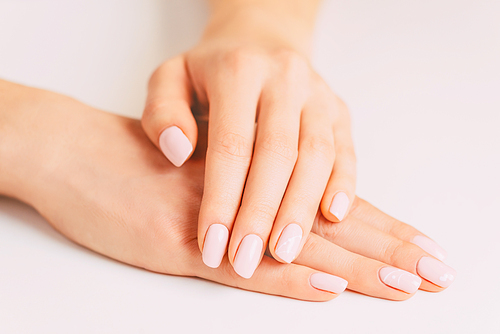 Beautiful young female hands with stylish manicure, nails of pastel pink color. Concept of beauty salon.