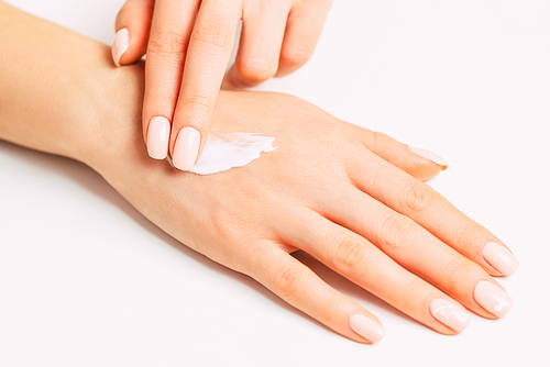 Woman’s hands with beautiful manicure applying moisturizing skincare cream.