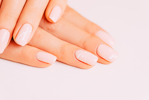 Closeup of female hands with beautiful manicure on a white background, nails of beige pastel color with art design. Concept of beauty salon.