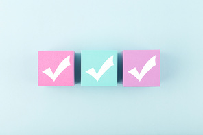 Three checkmarks on multicolored cubes in a row in the middle of bright pastel blue background. Concept of questionary, checklist, to do list, planning, business or verification. Modern minimal composition