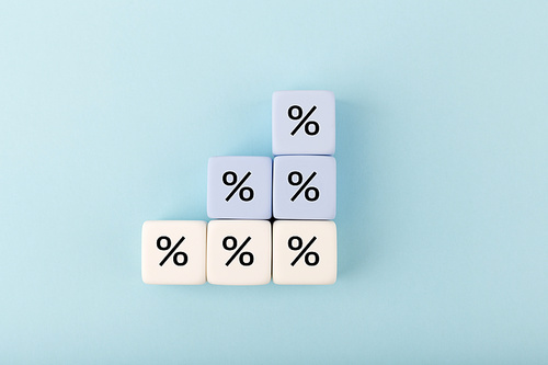 Toy blocks as a ladder with percentage sign on bright pastel blue background. Modern concept of inflation, percent, mortgage or interest rate growth