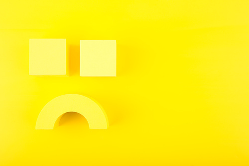 Creative flat lay with unhappy, sad smile symbol made of yellow figures on yellow background with copy space. Concept of emotions, emoji, mental health or unsatisfied customer