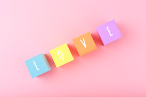 Word love written on colorful toy cubes against bright pink background with copy space. Minimal trendy concept of Valentine's day, love emotions, anniversary or dating