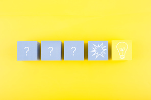 Concept of idea, creativity, start up or brainstorming. Light bulb and question signs drawn on toy cubes on yellow background