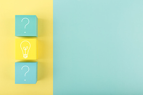 Concept of idea, creativity, start up or brainstorming. Light bulb and question signs drawn on toy cubes on yellow and blue background with copy space