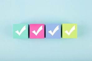 Four checkmarks on multicolored cubes in a row on blue background with copy space. Concept of questionary, checklist, to do list, planning, business or verification. Modern minimal composition