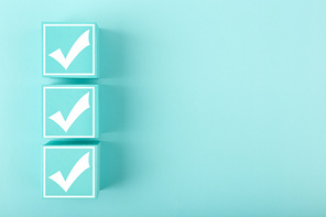 Three white checkmarks on toy cubes in a row on bright pastel blue background with copy space. Concept of questionary, kids related checklist, to do list, planning, business or verification.