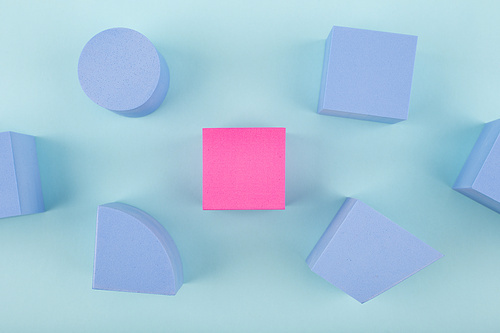 Pink cube and blue geometric figures on blue background. Concept of individuality, being different from others, leadership or unique ideas