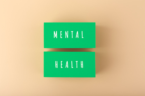 Creative flat lay with green tablets with written mental health text on bright beige background. Concept of world mental health day, mental health assessment and awareness