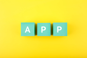 App written on blue cubes against bright yellow background. Modern, minimal concept of downloading apps for smartphone