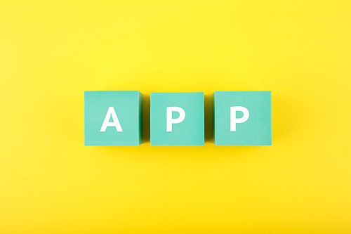 App written on blue cubes against bright yellow background. Modern, minimal concept of downloading apps for smartphone