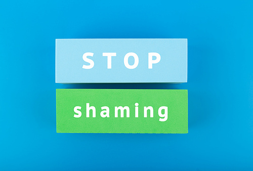 Stop shaming concept. Minimal flat lay with stop shaming inscription on blue and green rectangles on blue background.