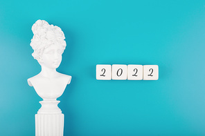 Creative trendy 2022 concept. Numbers written on white cubes next to white antique gypsum woman figure on mint blue background. New year resolution or plans concept