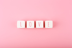 Word love written on white toy cubes against pink background with copy space. Minimal trendy concept of Valentine's day, love emotions, anniversary or dating