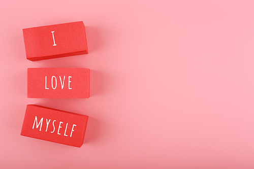 Minimal trendy concept of mental health and self love and acceptance. I love myself written on red toy rectangles in a row against bright pink background with copy space