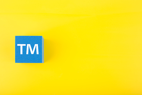 TM trademark sign on blue toy cube on yellow background with copy space. Concept of intellectual property registration and protection