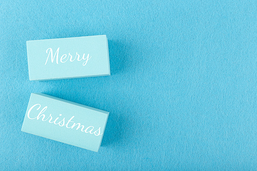 Merry Christmas minimal concept in light pastel blue colors. Handwritten text Merry Christmas on blue tablets against blue background with copy space. Modern trendy Merry Xmas concept