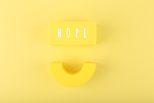 Creative optimistic concept of mental health, hope and faith. Smile and single word hope on bright yellow background