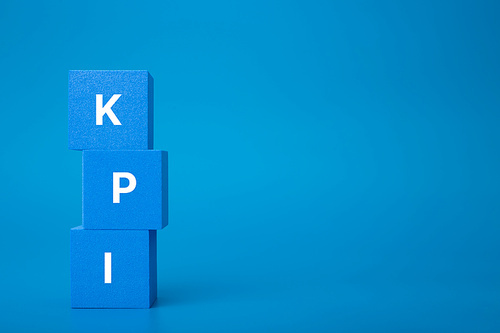 Minimal modern business KPI concept. KPI letters on stack of blue toy cubes against dark blue background with copy space.
