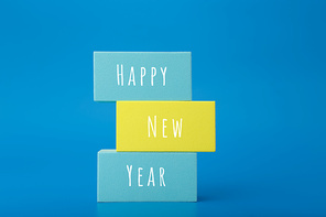 Happy New Year minimal trendy concept. Modern festive composition with stack of multicolored rectangles with written Happy New Year text against blue background