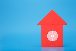Mortgage, loan or saving money for home and investing in real estate trendy concept. Red toy house with white target in the middle against blue background with copy space