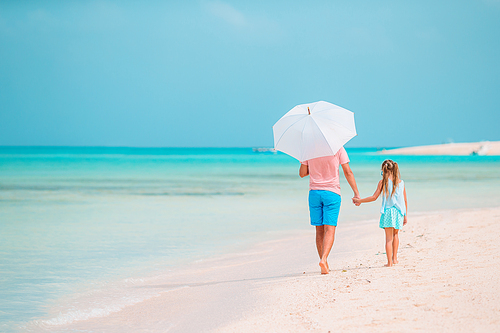 Family of father and little girl on tropical beach with umbrella for the sun