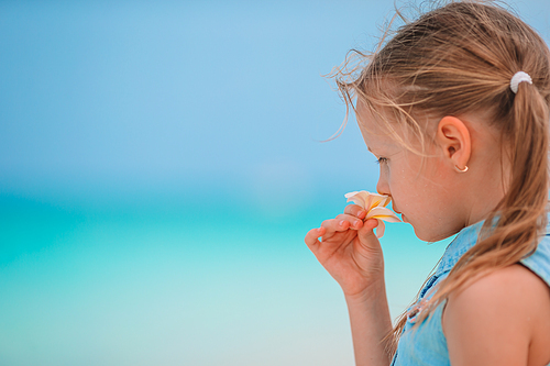 Adorable little girl enjoying smell of white beautiful frangipani flowers on the beach