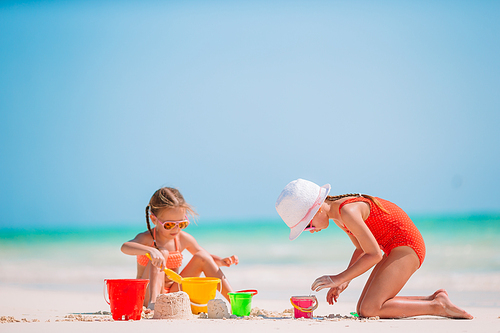 Little girls having fun at tropical beach playing together and making sandcastle