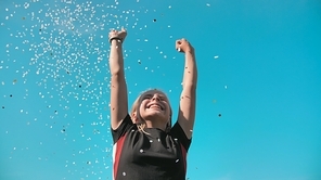 Success concept. Teen girl throws a multi-colored confetti into the blue sky