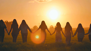 A group of girls walk towards the sun at sunset holding hands