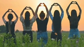 Five girls make a heart shape from their hands at sunset