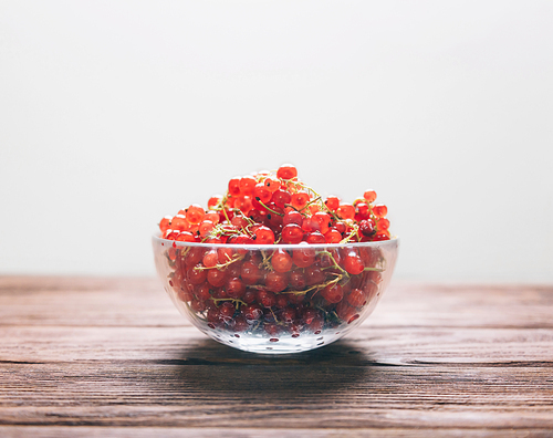 Fresh red currant in a glass bowl on a wooden background, side view. Copy-space in upper part of image.