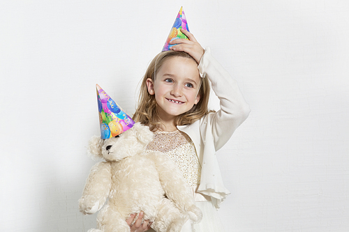 Happy young birthday girl wearing party hat with teddy bear over colored background