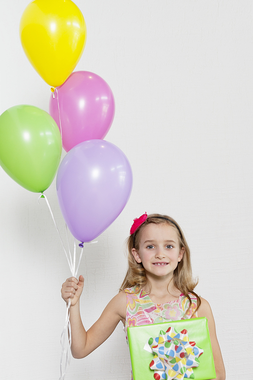 Portrait of a happy girl with party balloons and gift over colored background