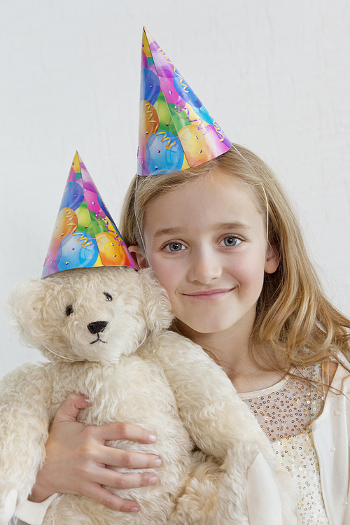 Portrait of a happy young girl wearing party hat with soft toy over colored background