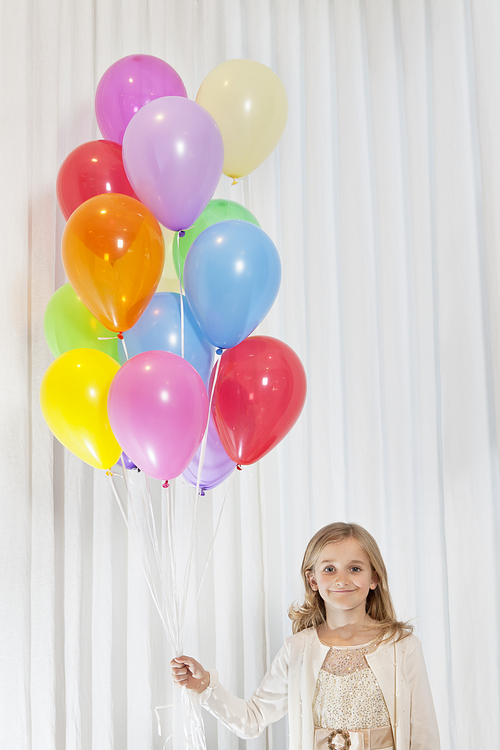 Portrait of young birthday girl standing with party balloons