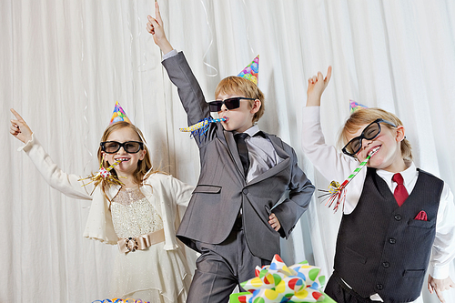 Brothers and sister wearing sunglasses and party puffer in mouth dancing