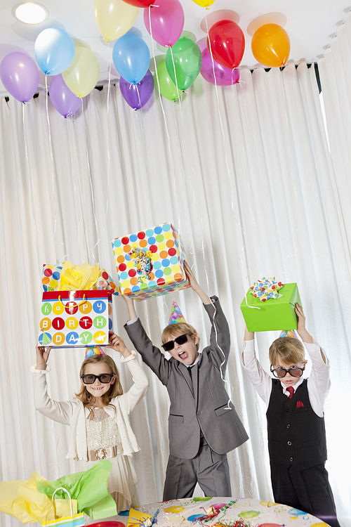 Brothers and sister wearing sunglasses holding gift aloft while shouting