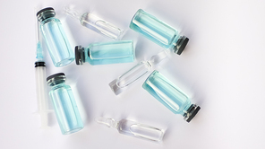 Vial vaccine, top view of glass ampoules with transparent and blue liquid lying on white background, global vaccination concept.