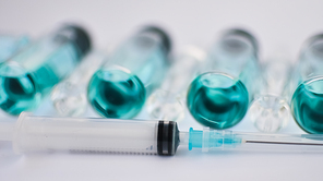 Vial vaccine, top view of glass ampoules with transparent and blue liquid, a syringe is lying near on white background, global vaccination concept.