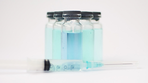 Vial vaccine, glass ampoules with transparent and blue liquid, a syringe is lying near on white background, global vaccination concept.