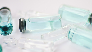 Vial vaccine, top view of glass ampoules with transparent and blue liquid lying on white background, global vaccination concept.