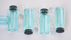 Vial vaccine, top view of glass ampoules with transparent and blue liquid lying on white background, global vaccination concept.