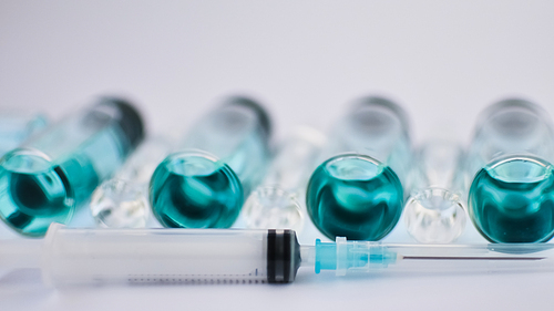 Vial vaccine, top view of glass ampoules with transparent and blue liquid, a syringe is lying near on white background, global vaccination concept.