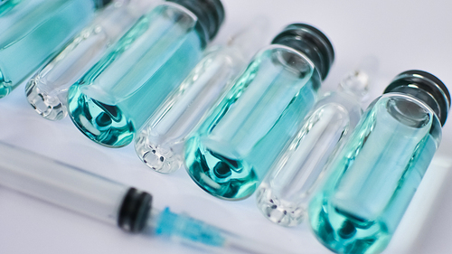 Vial vaccine, top view of glass ampoules with transparent and blue liquid, a syringe is lying near on white background, global vaccination concept.